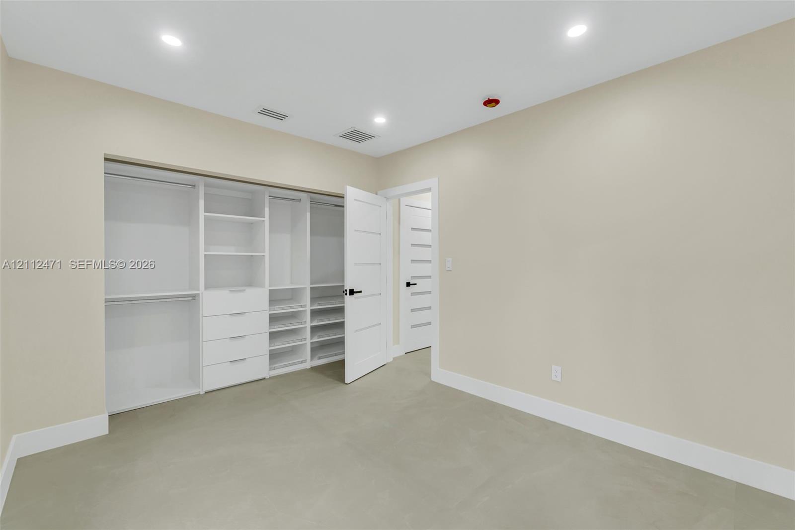 Customized walk-in closet featuring floor-to-ceiling white cabinetry, integrated drawer storage, and multiple shelving units, complemented by solid-core interior doors with matte black hardware and recessed lighting