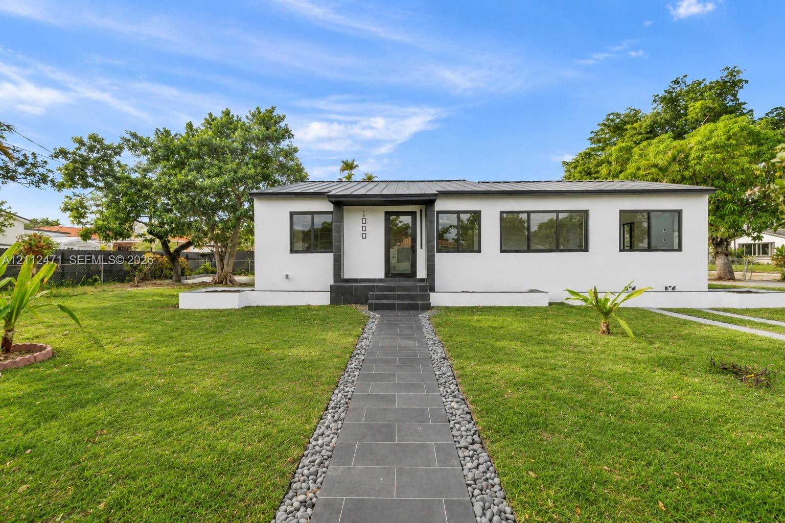 Single-story exterior featuring a metal roof, white stucco facade, dark-toned tile entryway, and large-pane windows