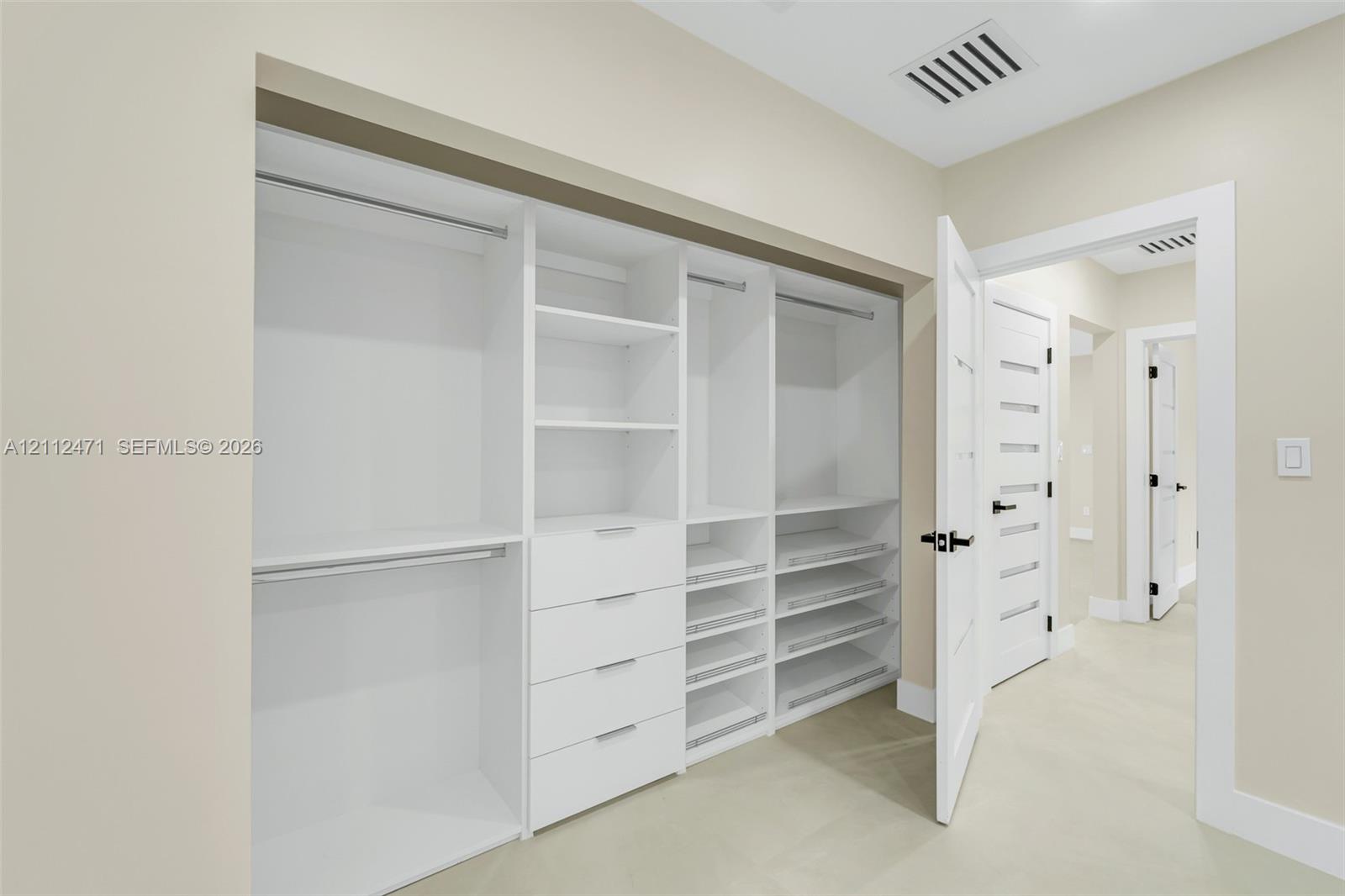 Custom built-in closet featuring floor-to-ceiling white shelving, integrated drawers, pull-out storage racks, and dual hanging rods