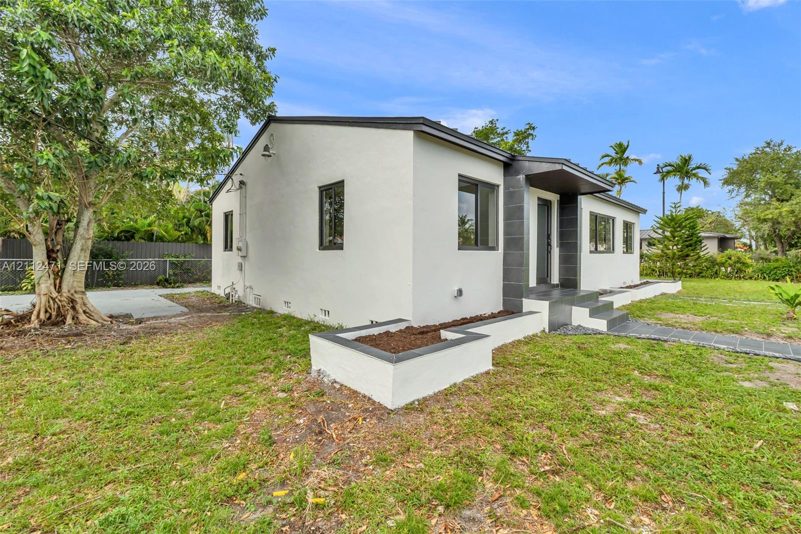 Single-story exterior featuring light-toned stucco siding, dark-toned masonry accents, a raised concrete entryway, a built-in garden planter, and a tiled walkway Single-story exterior featuring light-toned stucco siding, dark-toned masonry accents, a raised concrete entryway, a built-in garden planter, and a tiled walkway