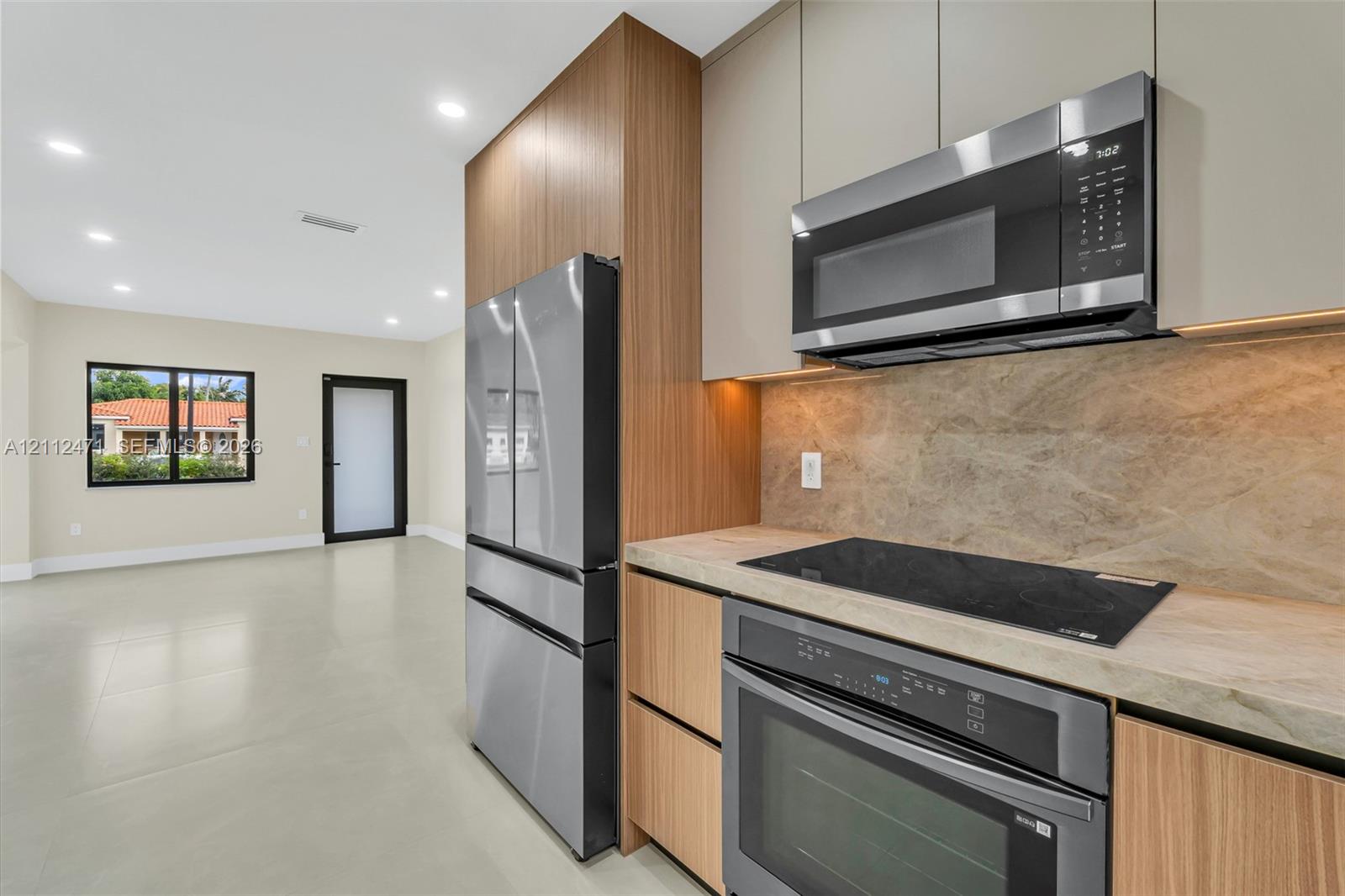 Modern kitchen featuring slab-front cabinetry, stone-patterned backsplash, stainless steel appliances, and integrated under-cabinet lighting