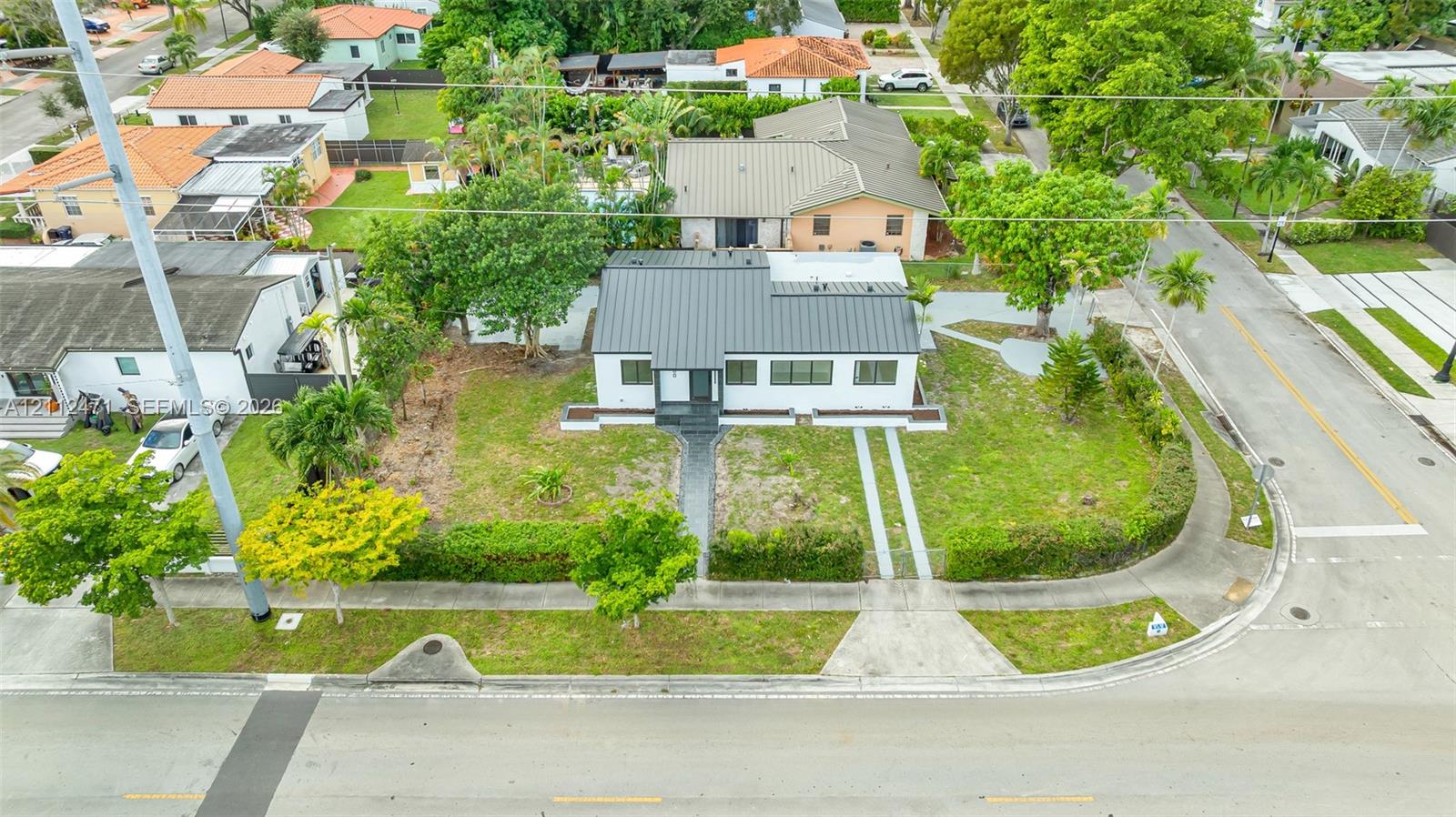 Corner lot residence featuring a standing-seam metal roof, white exterior siding, manicured hedges, and dual concrete driveway strips