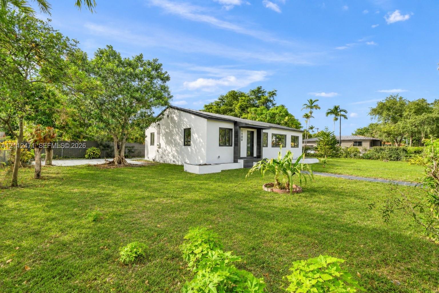 Single-story residence featuring a smooth white stucco exterior, dark-toned window trim, an expansive grass lawn, and mature canopy trees Single-story residence featuring a smooth white stucco exterior, dark-toned window trim, an expansive grass lawn, and mature canopy trees