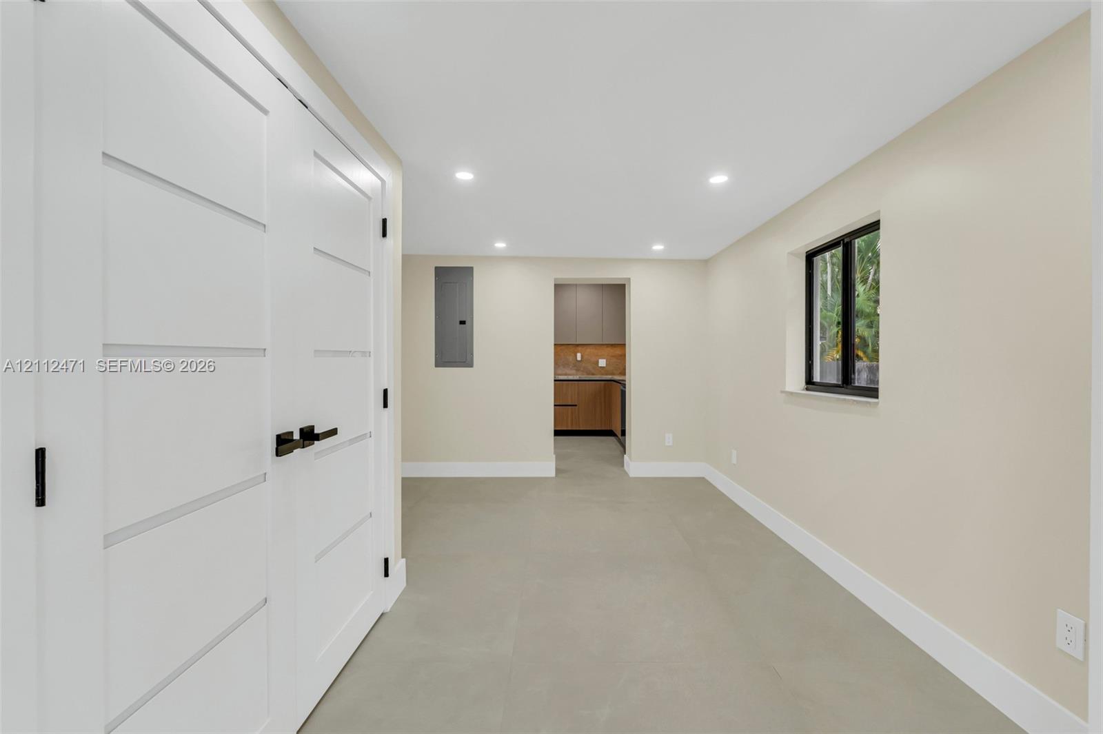 Neutral-toned interior featuring recessed lighting, large-format tile flooring, a window with a dark frame, and white shaker-style double doors with matte black hardware