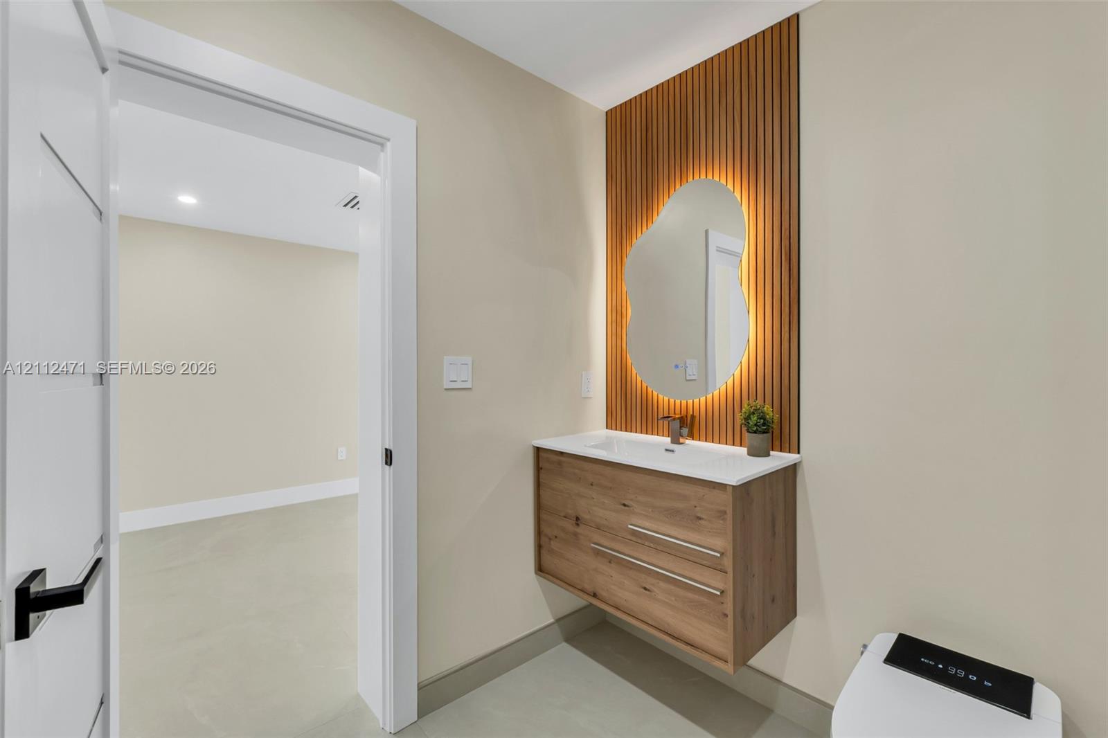 Floating wood-finish vanity with a white countertop, organic-shaped backlit mirror, and vertical wood slat wall accent