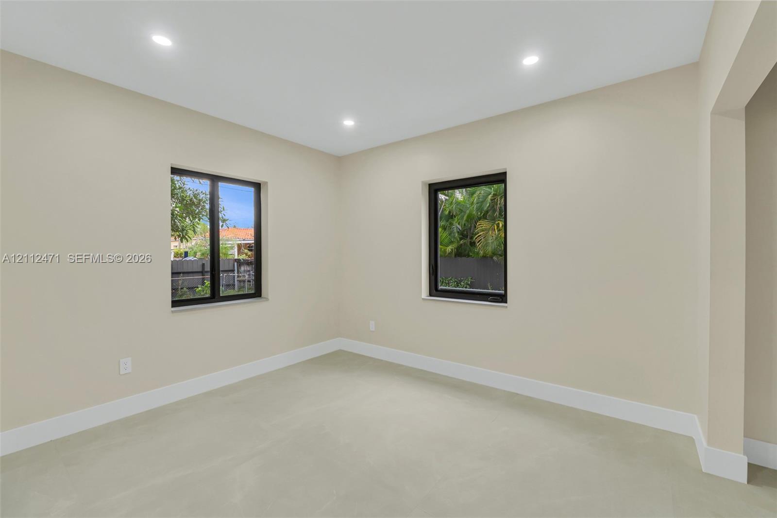 Neutral-toned interior room featuring large windows with dark frames, light-colored tile flooring, and recessed ceiling lighting