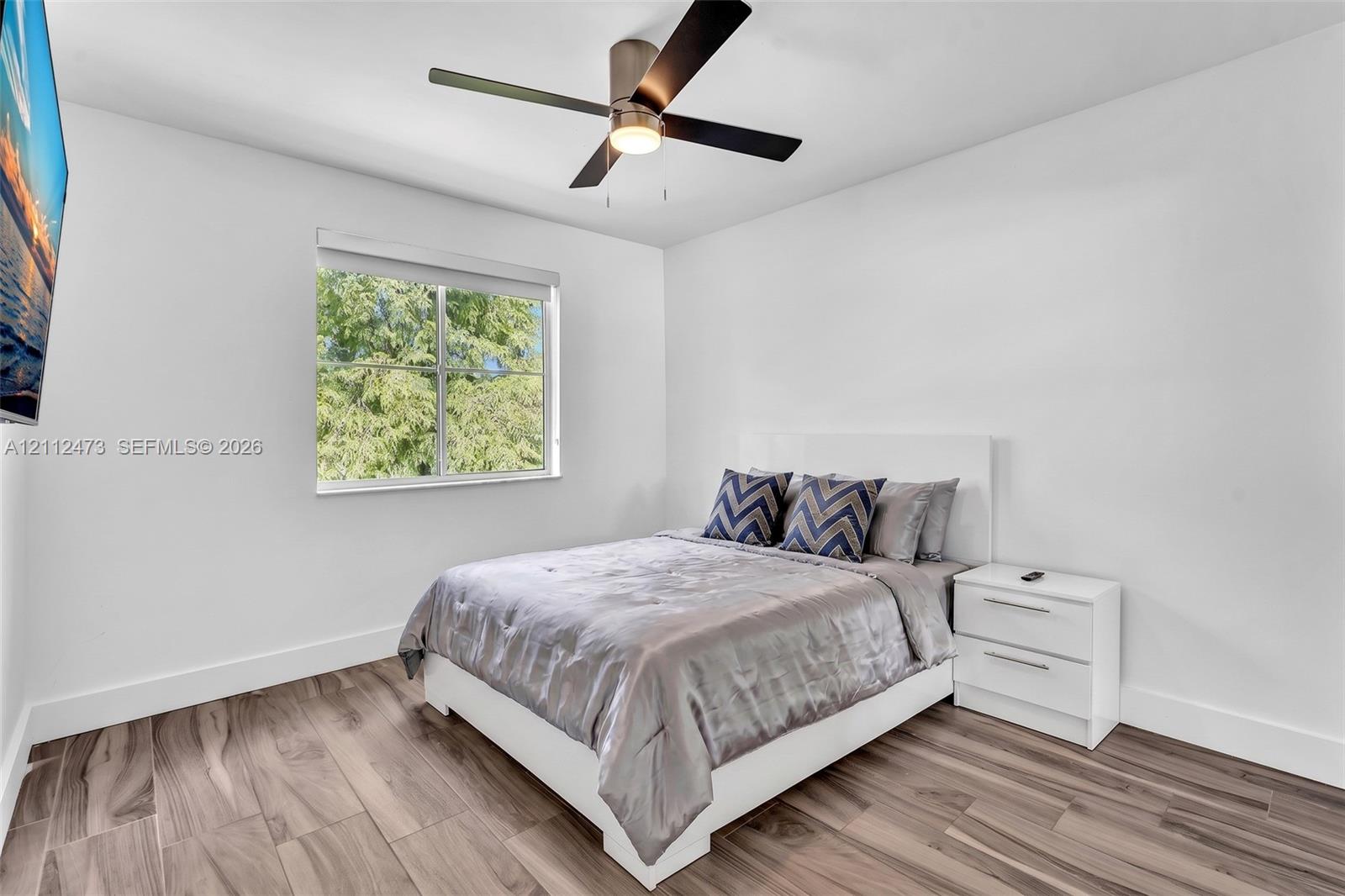 Bedroom featuring wood-finish flooring, a contemporary ceiling fan with integrated lighting, and a single-pane window