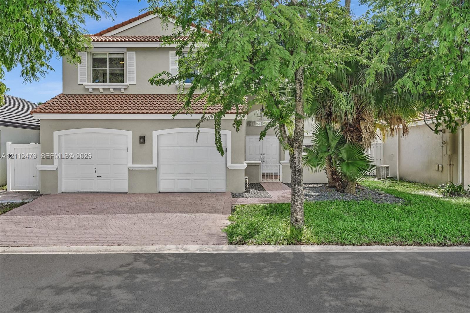 Two-story residence featuring a tile roof, dual-bay garage, paved driveway, and double-entry doors Two-story residence featuring a tile roof, dual-bay garage, paved driveway, and double-entry doors