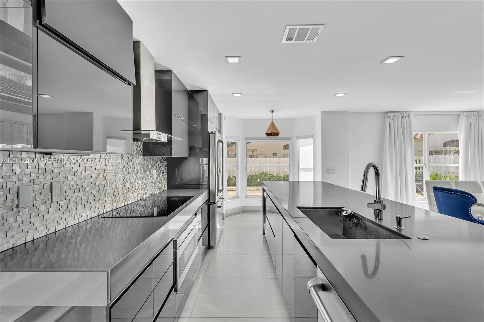 Modern kitchen featuring high-gloss cabinetry, stone countertops, a mosaic tile backsplash, a stainless steel range hood, and a large central island with an undermount sink