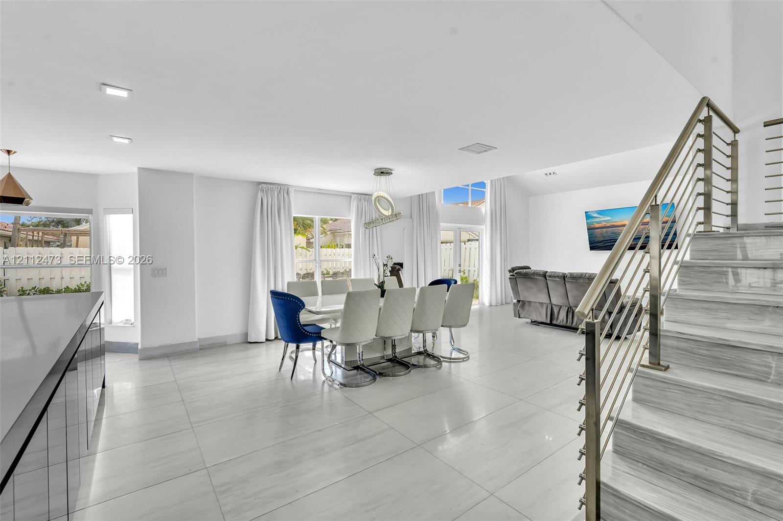 Open-concept interior featuring large-format tile flooring, vaulted ceilings, recessed lighting, and a staircase with stainless steel cable railing