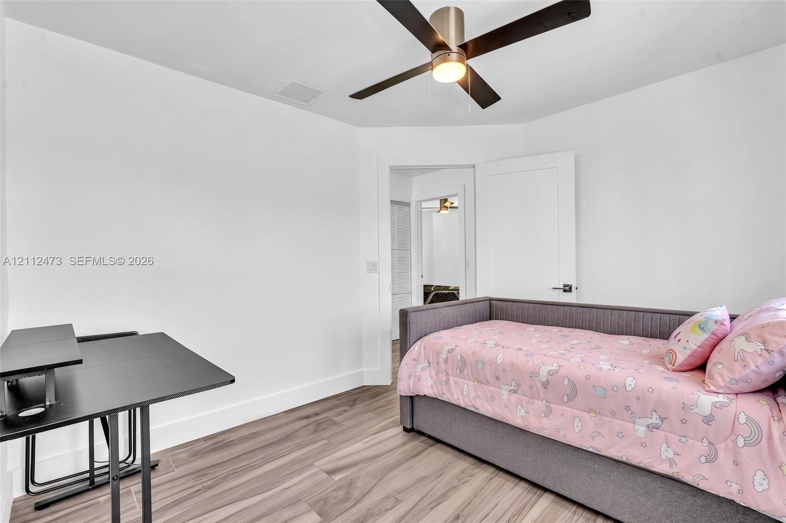 Room featuring wood-finish flooring, white walls, and a ceiling fan with integrated lighting