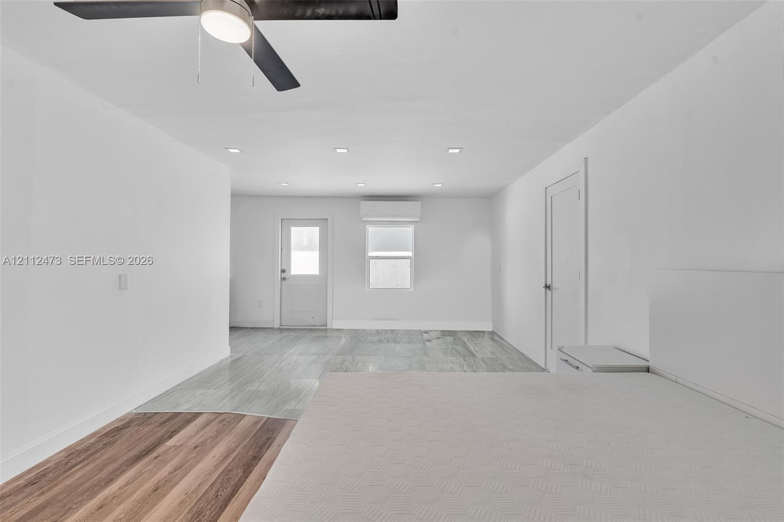 Interior space featuring mixed-material wood-finish flooring, recessed lighting, a modern ceiling fan, and a wall-mounted climate control unit