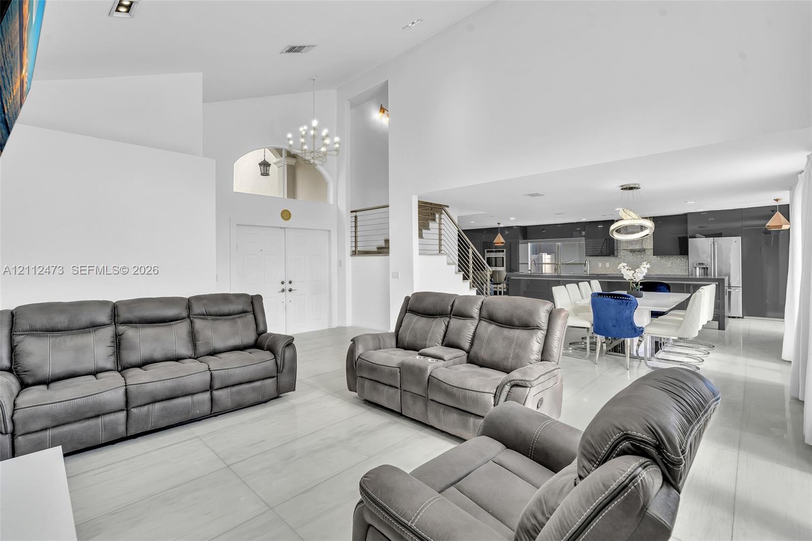 Vaulted ceilings, large-format tile flooring, a built-in staircase with a metal railing, recessed lighting, and a modern kitchen featuring a central island