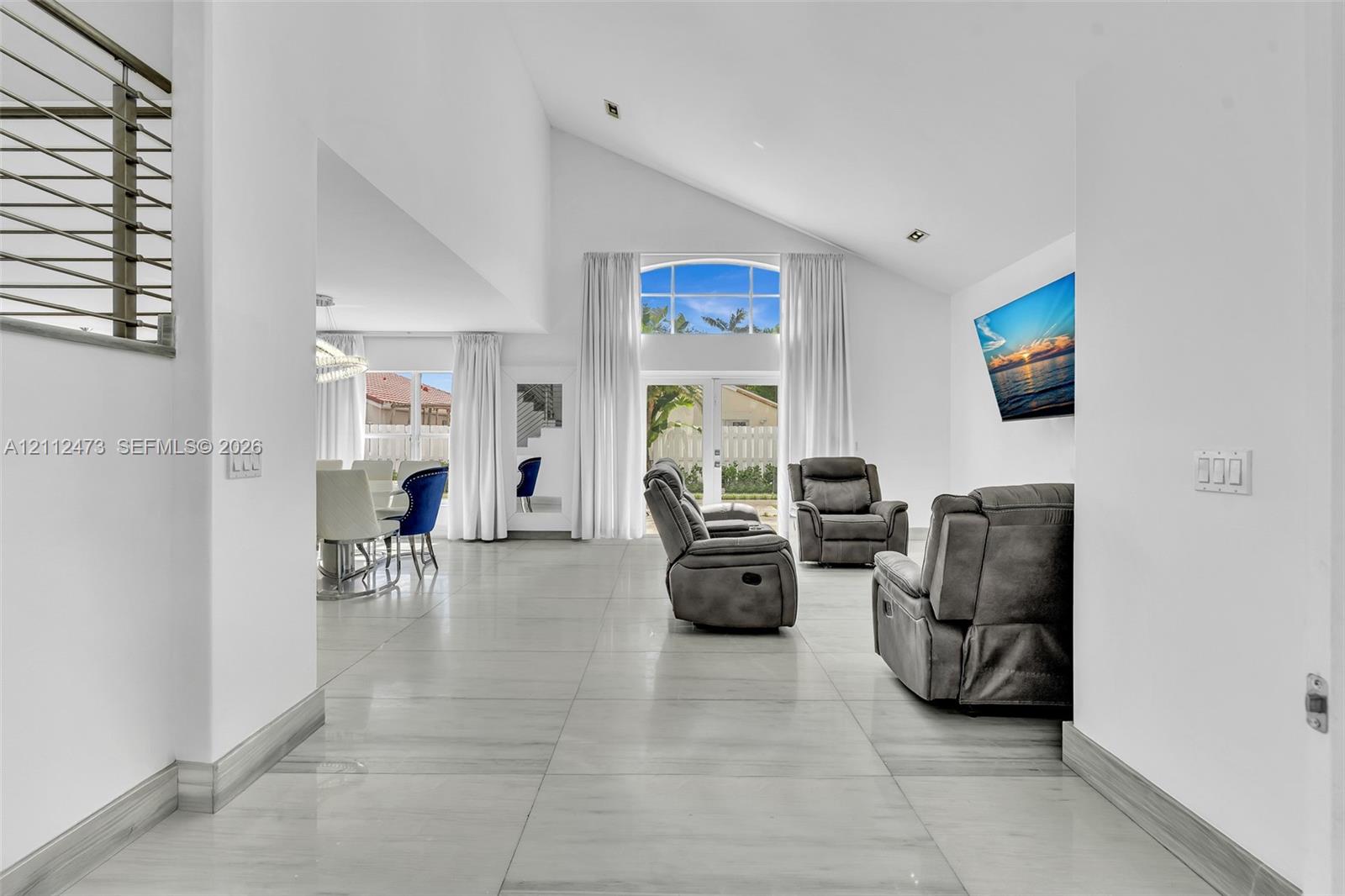 Vaulted ceilings, large-format tile flooring, double-door glass entrance with arched transom window, and metal cable railing