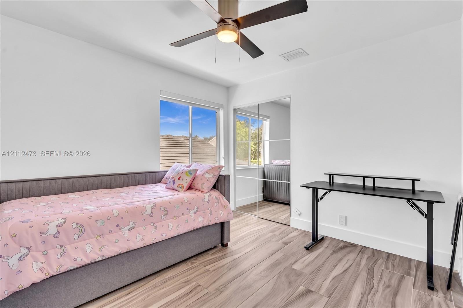 Room featuring wood-finish flooring, a ceiling fan with integrated lighting, dual-pane windows, and a sliding mirrored closet door