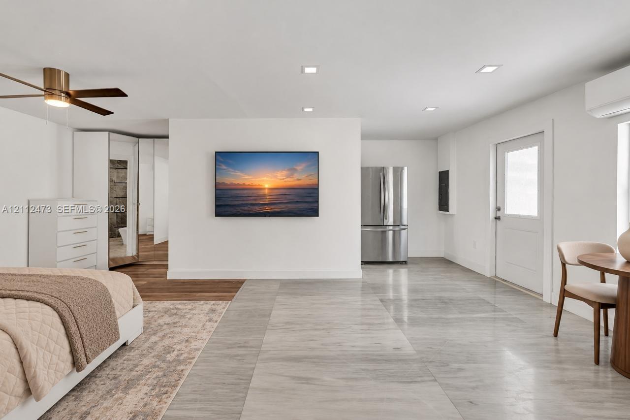 Light-toned tile flooring, recessed ceiling lighting, brushed metallic ceiling fan, stainless steel refrigerator, and wall-mounted climate control unit