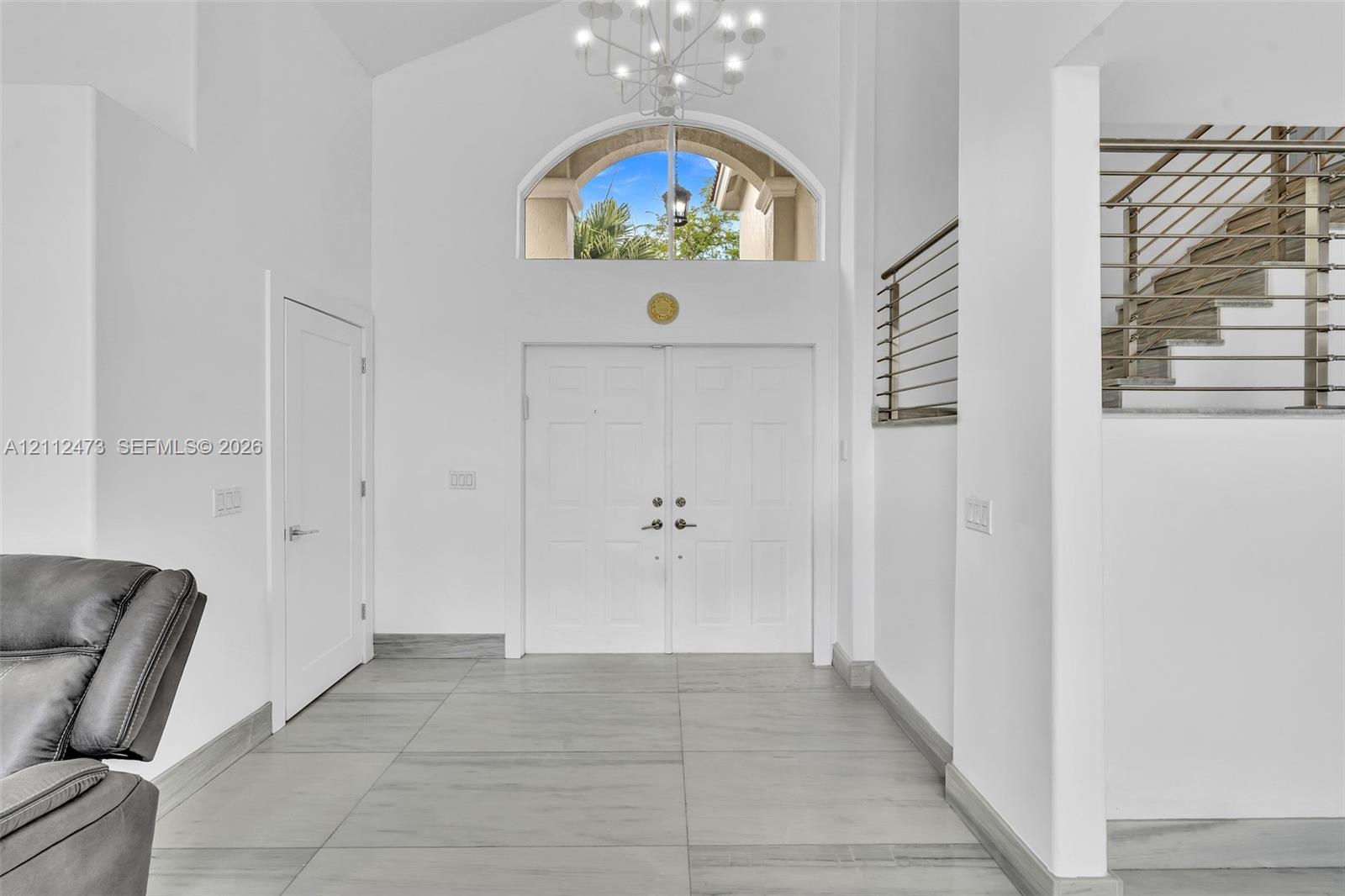 Double-door entryway featuring vaulted ceilings, a prominent arched transom window, a contemporary multi-arm chandelier, and metal horizontal-bar railing