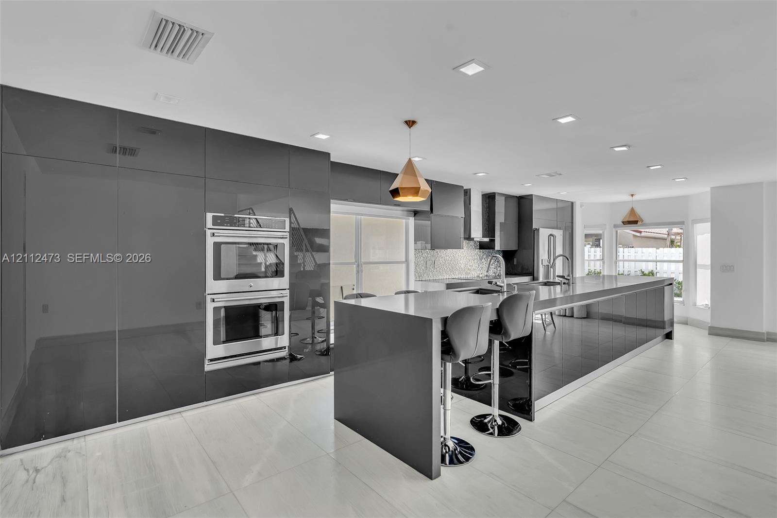 Contemporary kitchen featuring high-gloss cabinetry, stainless steel double wall ovens, a large kitchen island with quartz countertops, recessed lighting, and large-format tile flooring
