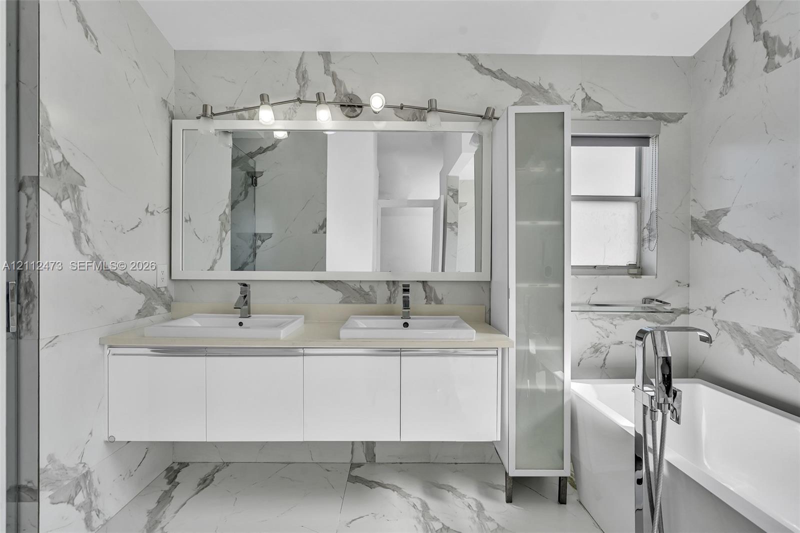 Floating double vanity with integrated rectangular sinks, stone-finish countertop, full-height frosted glass cabinetry, and floor-to-ceiling vein-patterned tile wall cladding
