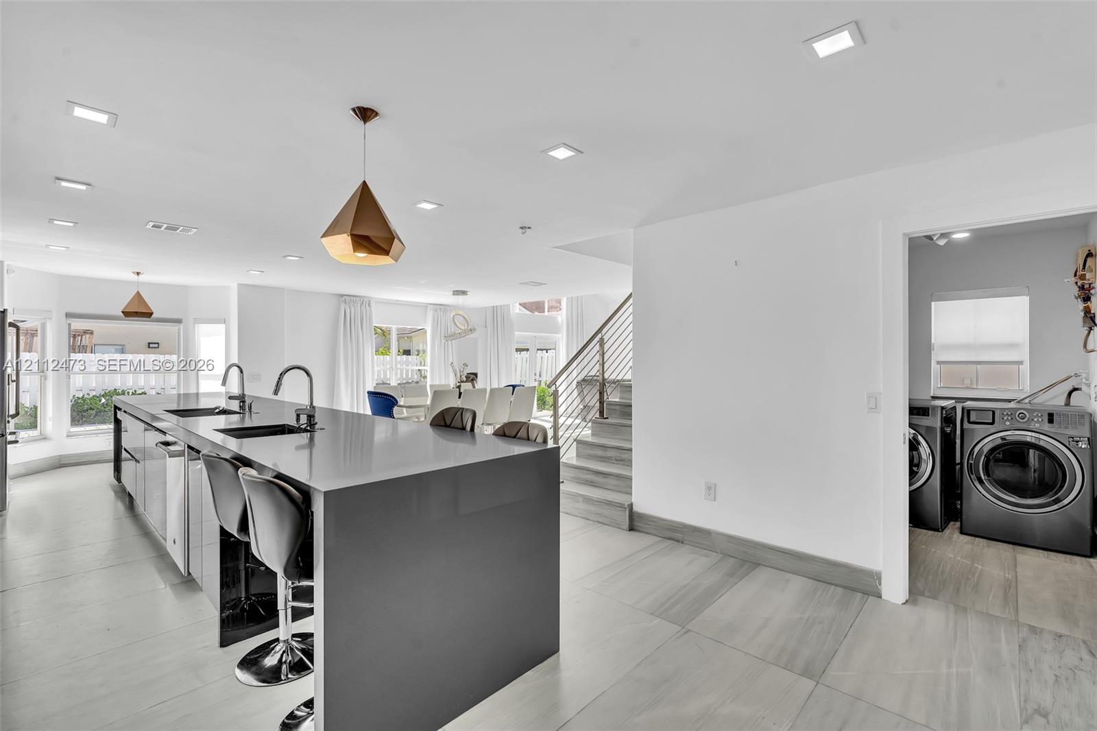 Kitchen featuring a large island with a solid surface countertop, dual undermount sinks, geometric pendant lighting, and tile flooring