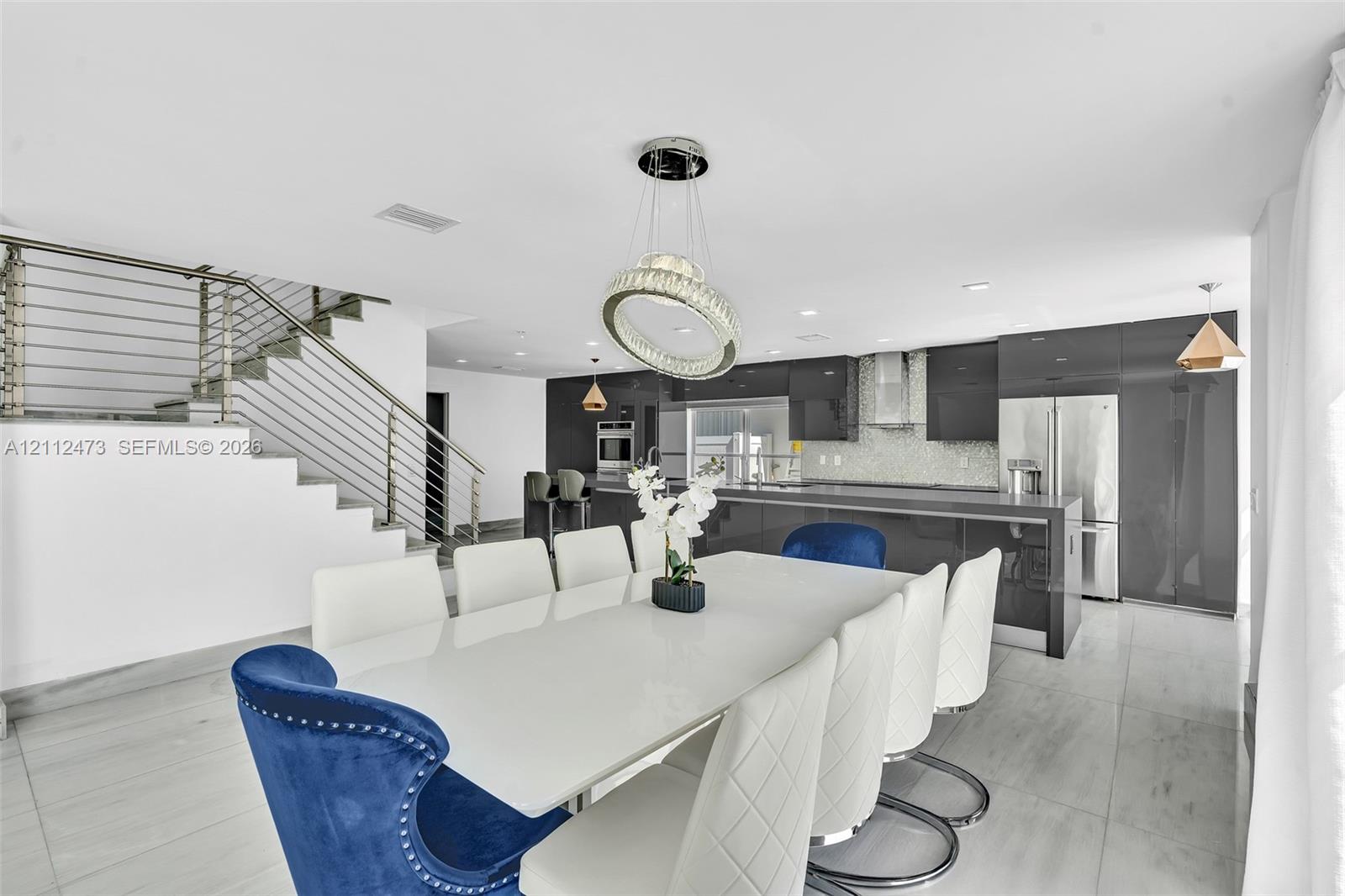 Open-concept kitchen featuring high-gloss dark cabinetry, integrated stainless steel appliances, and tile flooring