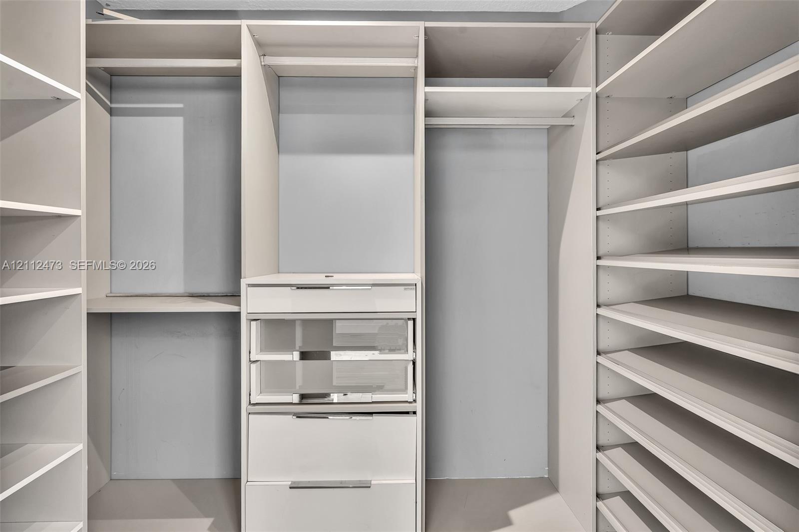 Customized closet organization system featuring adjustable shelving, integrated garment rods, and built-in drawers with glass-front paneling