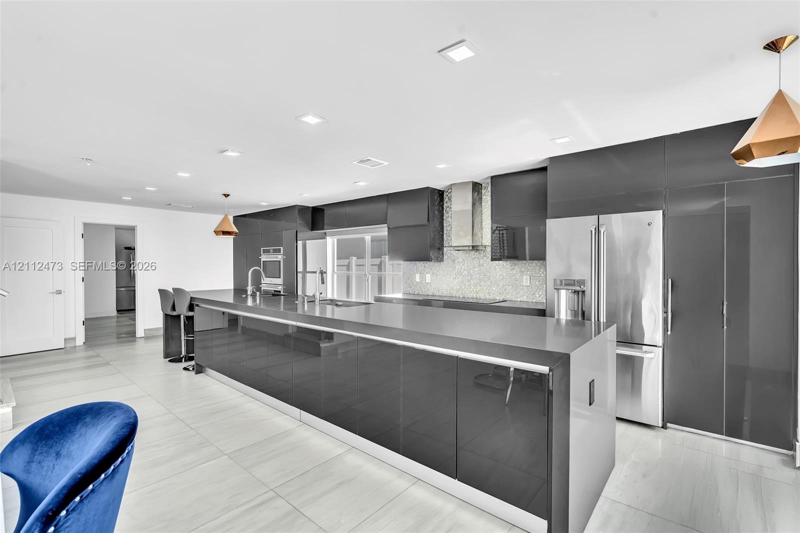 Contemporary kitchen featuring high-gloss cabinetry, stainless steel appliances, a stone countertop island, recessed lighting, and large-format tile flooring