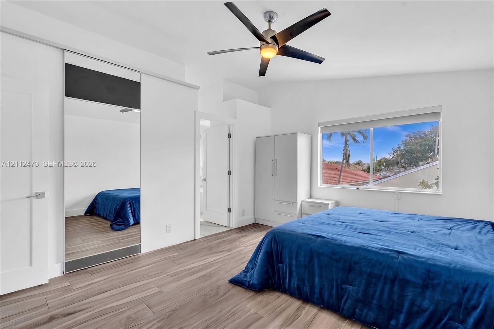 Room featuring wood-finish flooring, vaulted ceilings, a ceiling fan, and sliding mirror-panel closet doors