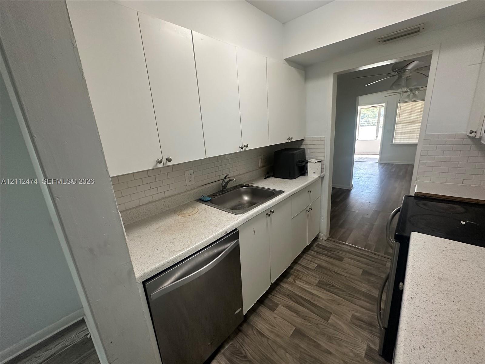 Kitchen featuring white cabinetry, light-toned countertops, subway tile backsplash, stainless steel dishwasher, and wood-finish flooring