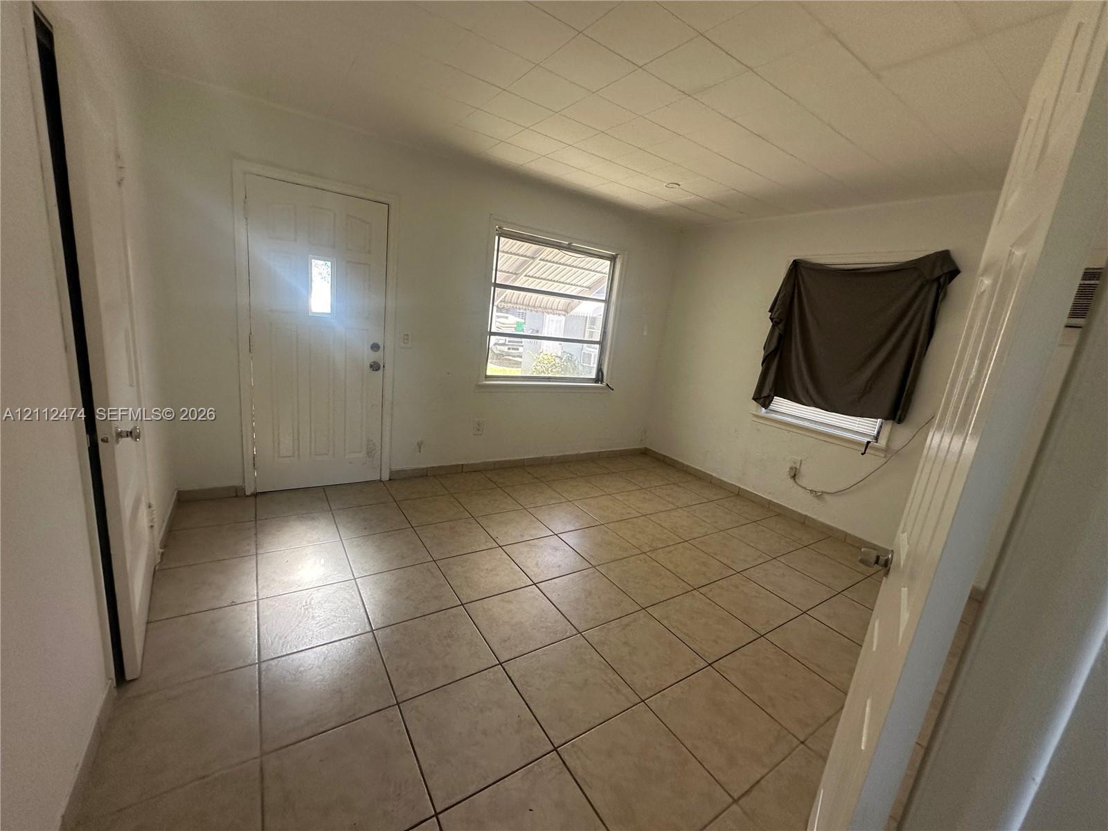 Interior space featuring neutral tile flooring, a multi-pane entry door, dual windows with exterior framing, and a segmented ceiling Interior space featuring neutral tile flooring, a multi-pane entry door, dual windows with exterior framing, and a segmented ceiling