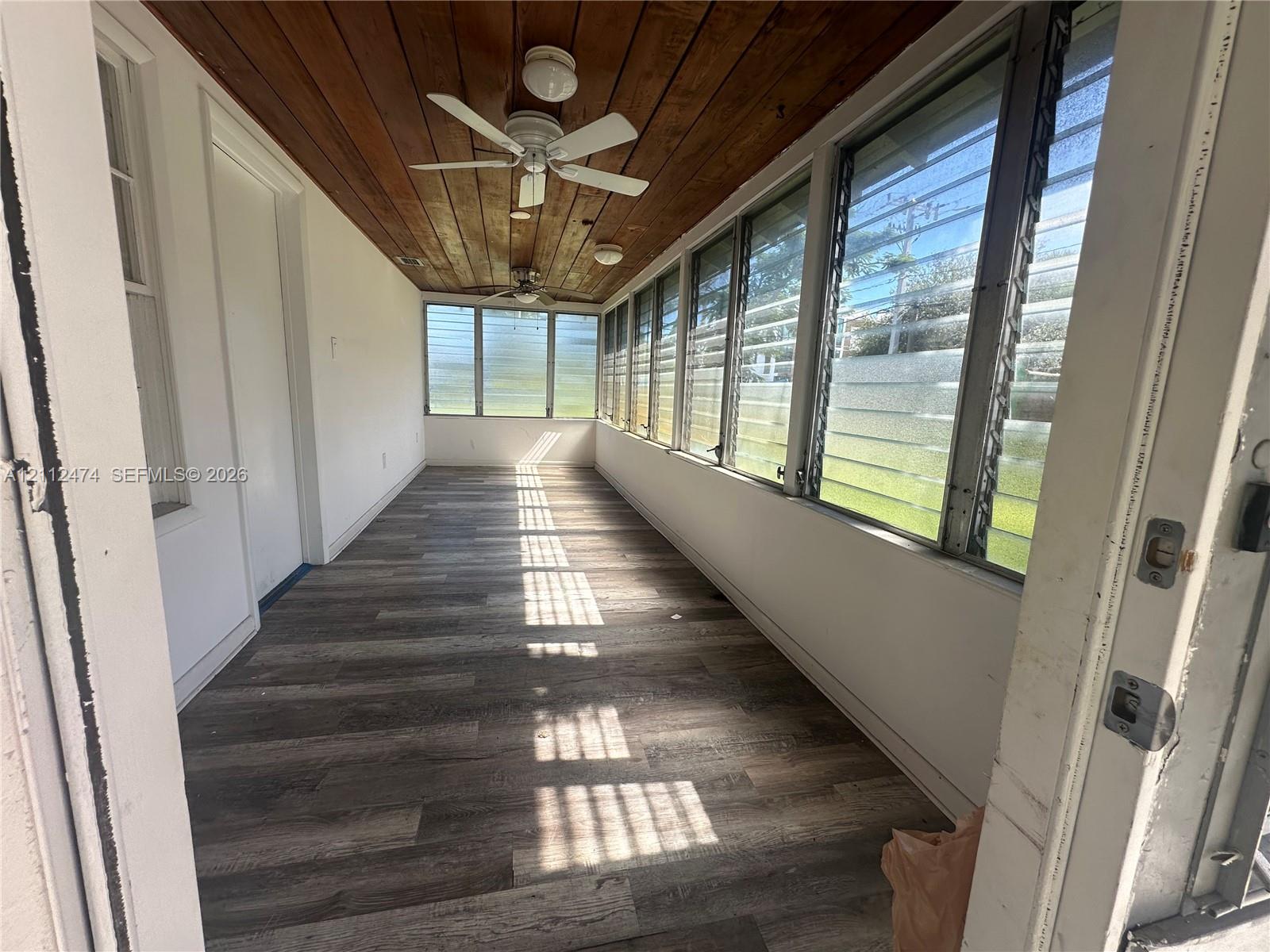 Enclosed porch featuring wood-finish plank flooring, wood-paneled ceiling, adjustable louvered windows, and ceiling-mounted fans