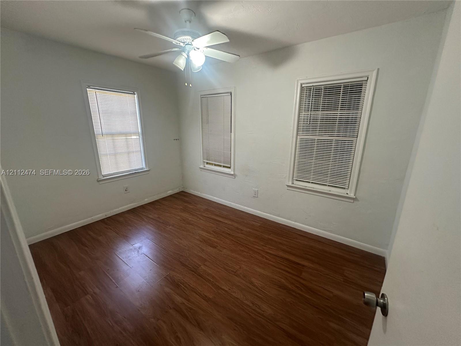 Room featuring wood-finish flooring, three double-hung windows, and a ceiling fan with integrated lighting