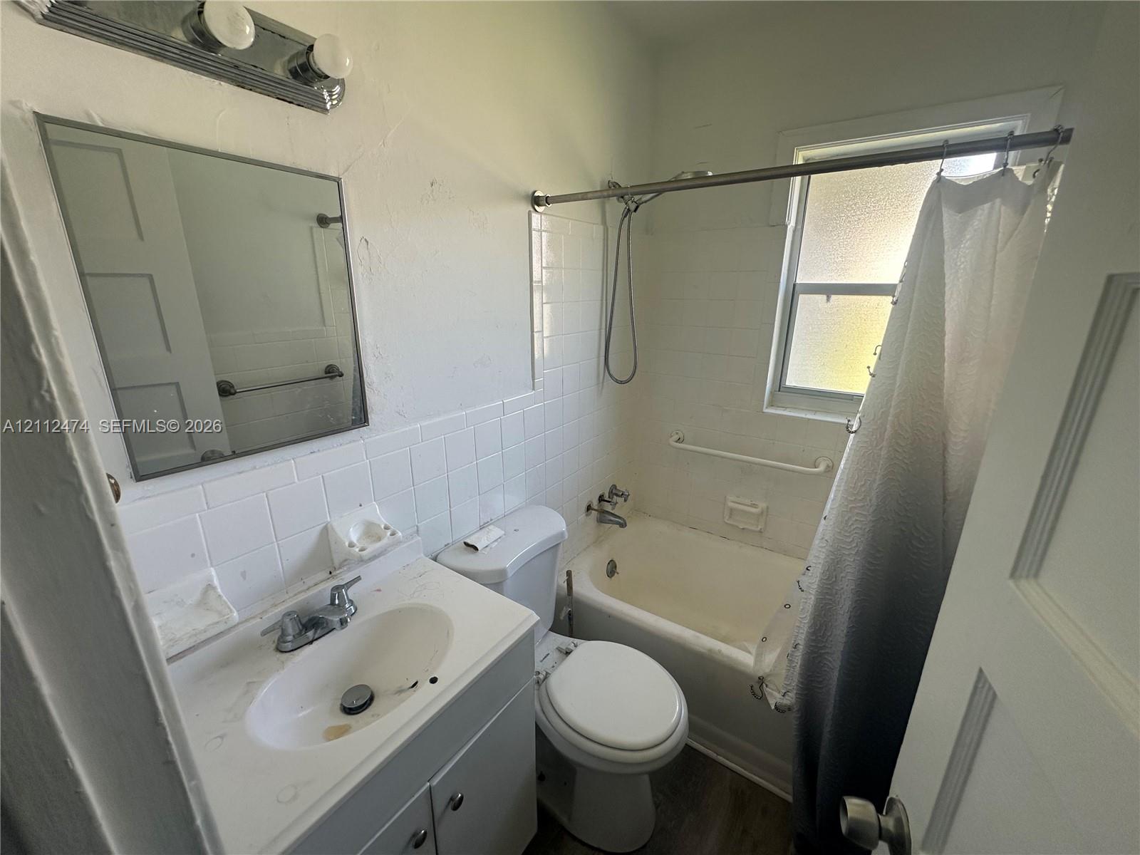 Bathroom featuring a vanity with integrated basin, wall-mounted vanity mirror, white tile shower surround, and a double-light fixture