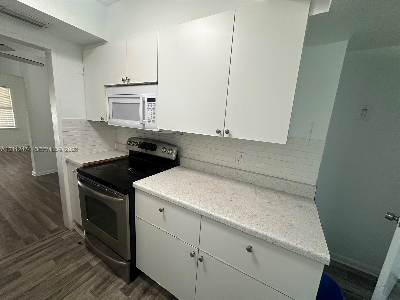 Kitchen featuring white cabinetry, solid-surface countertops, subway tile backsplash, and stainless steel appliances including a range and over-the-range microwave