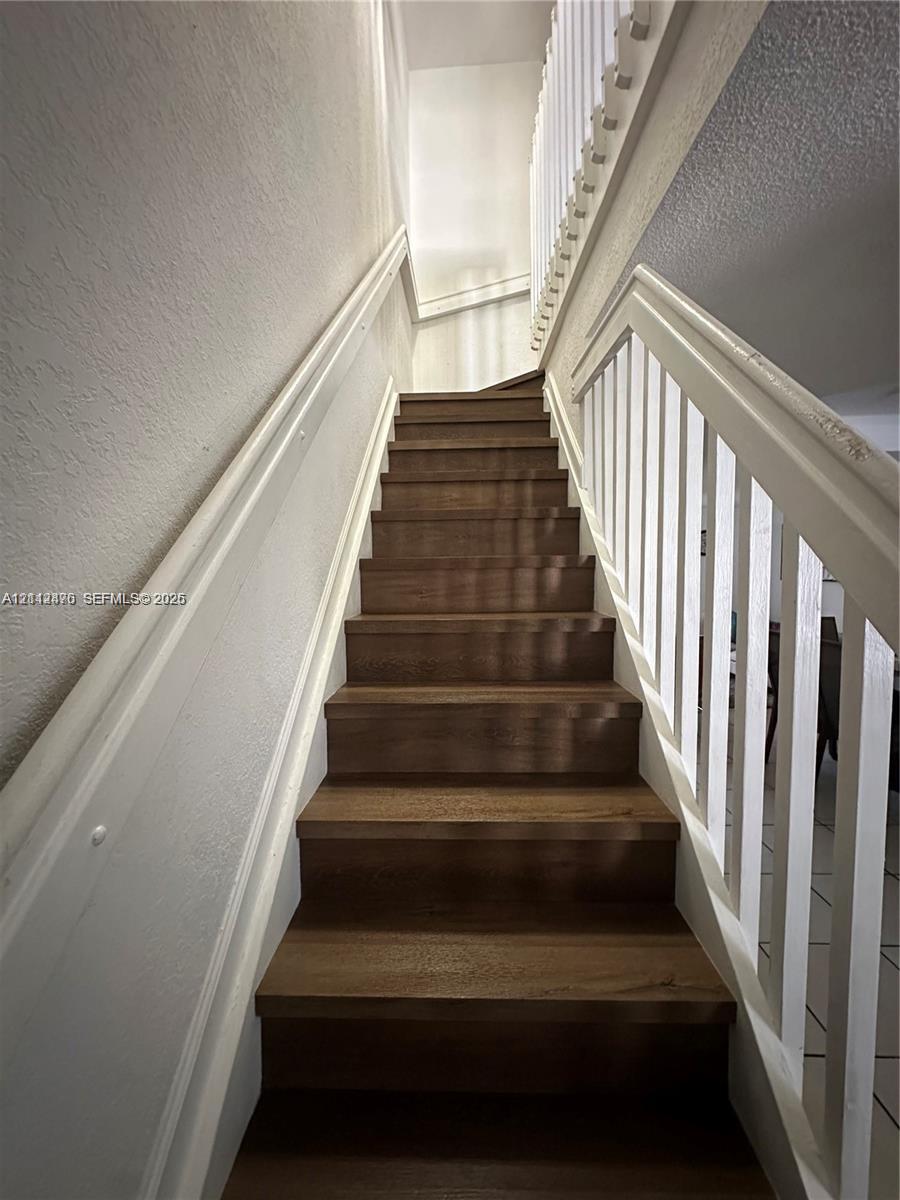 Staircase featuring wood-finish treads, white handrails, and vertical balusters