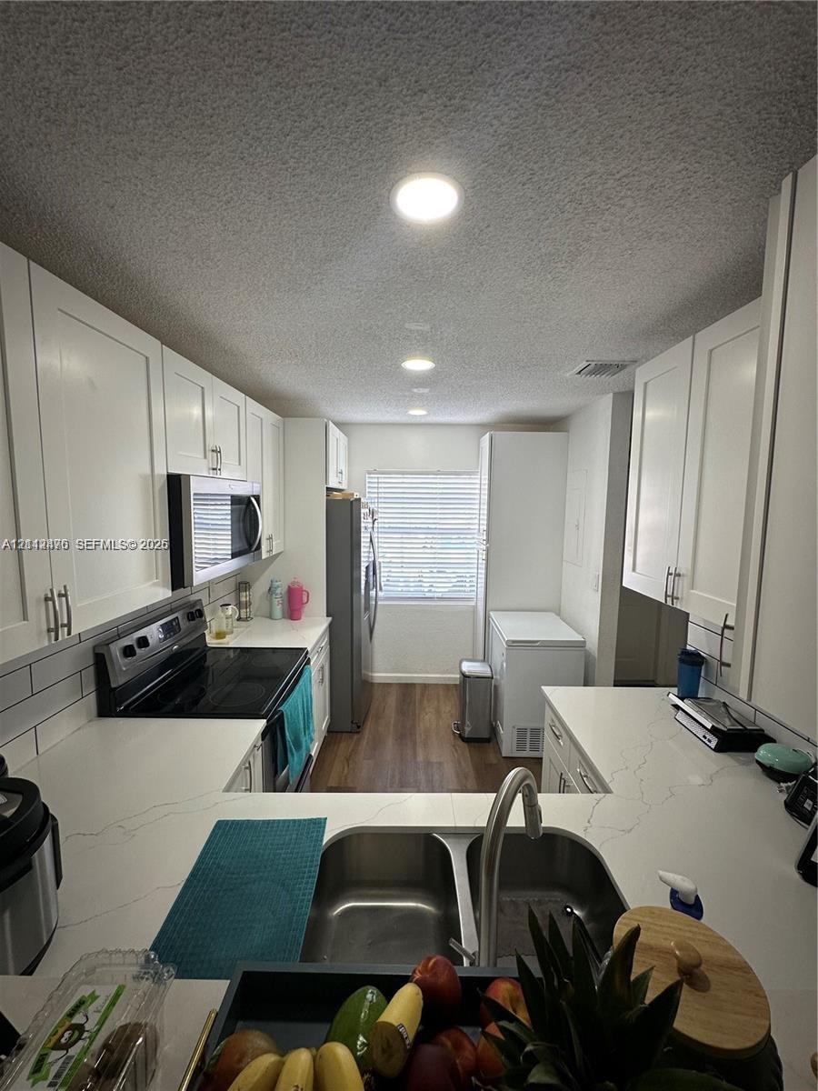 Kitchen featuring white shaker-style cabinetry, white countertops with grey veining, stainless steel undermount double-basin sink, subway tile backsplash, and wood-finish flooring