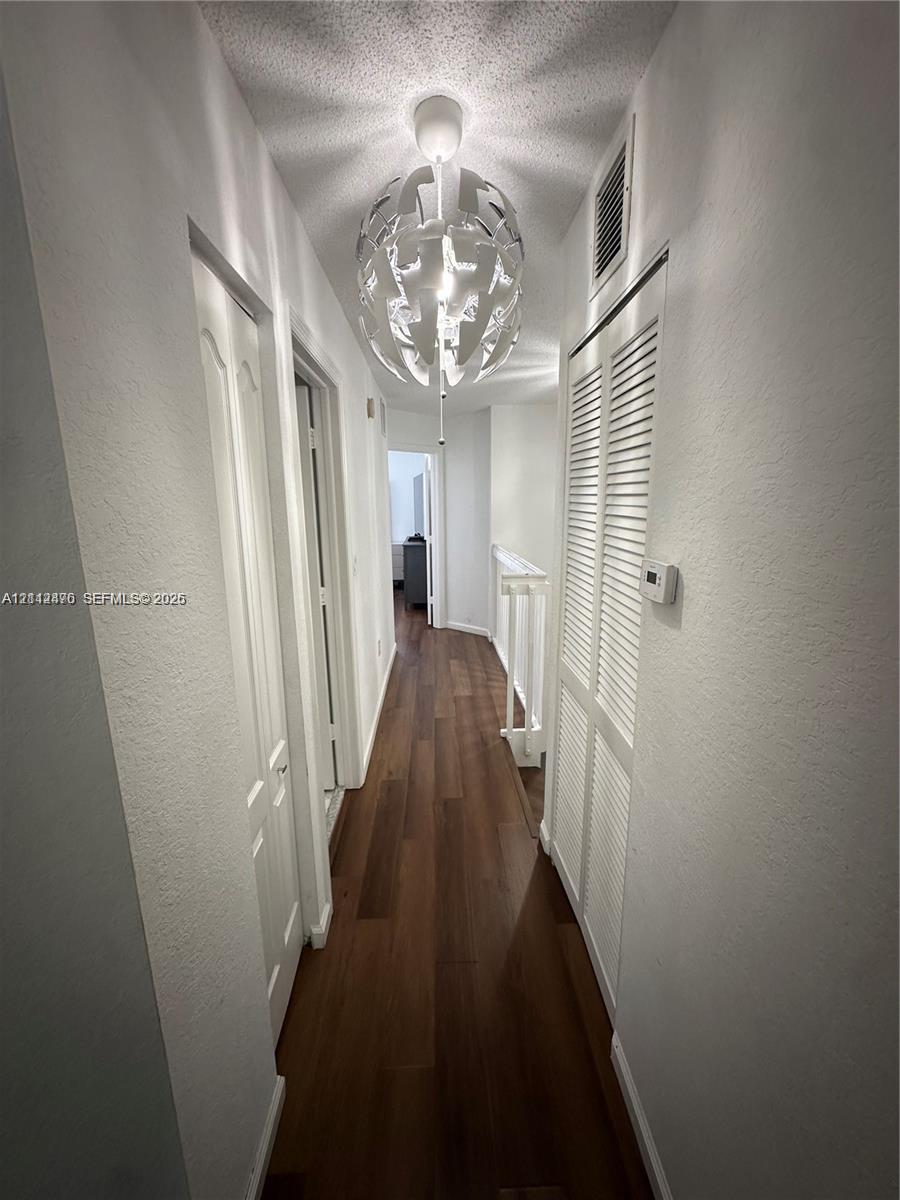 Hallway featuring wood-finish flooring, a geometric spherical pendant light fixture, and double louvered closet doors