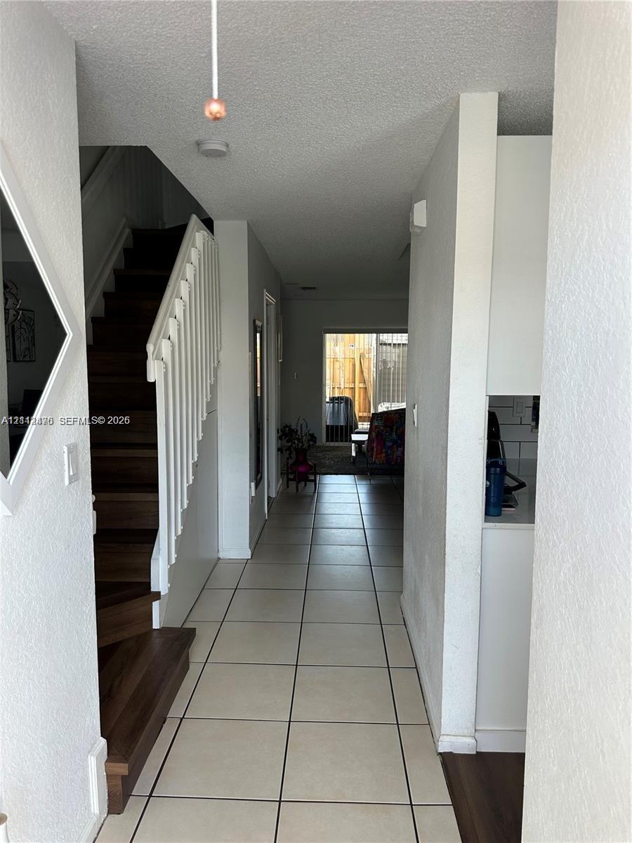 Interior hallway featuring ceramic tile flooring, a staircase with wood-finish treads, and a white balustrade