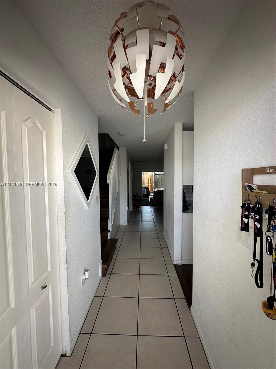 Entryway featuring ceramic tile flooring, a geometric multi-panel pendant light fixture, and a decorative diamond-shaped wall inlay
