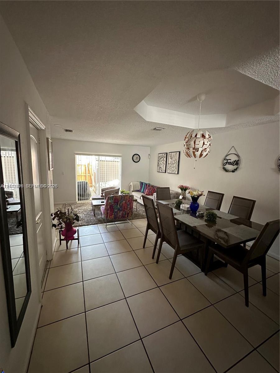 Neutral tile flooring, coffered ceiling with a pendant light fixture, and glass sliding doors leading to the exterior