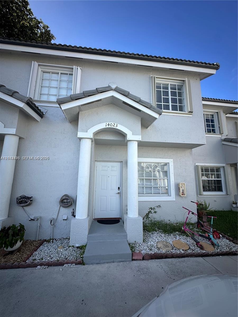 Two-story stucco exterior featuring a covered entryway with structural columns, multi-pane windows, and a dedicated concrete pathway Two-story stucco exterior featuring a covered entryway with structural columns, multi-pane windows, and a dedicated concrete pathway