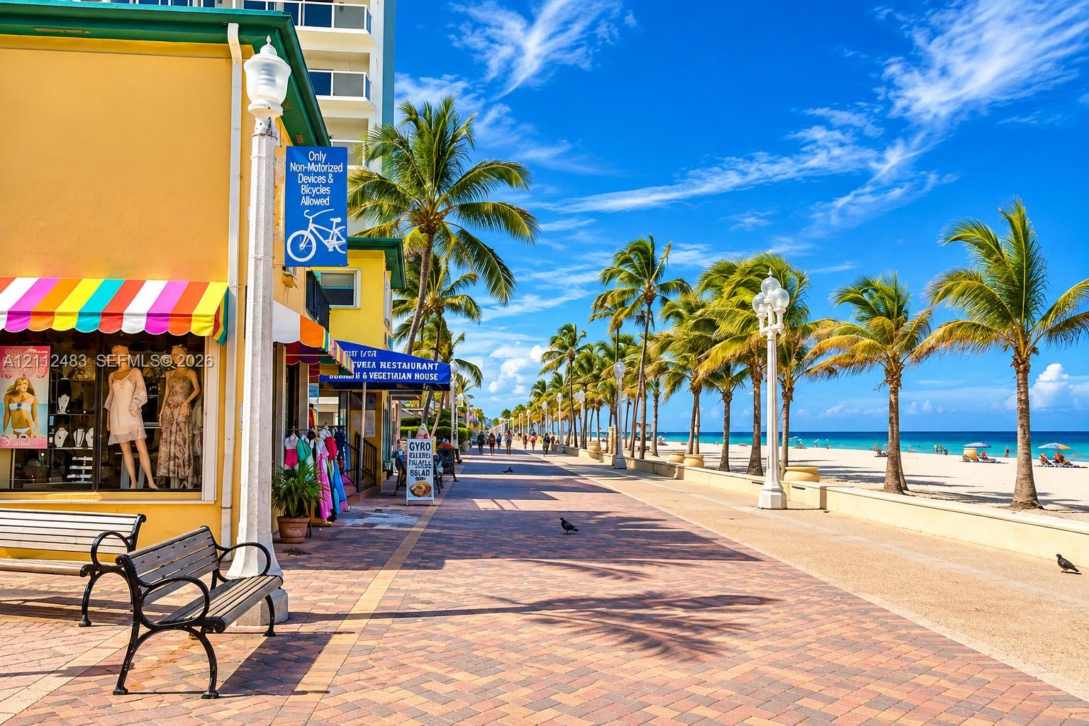 Paved brick promenade featuring ornate street lighting, mature palm trees, and direct access to a sand beach