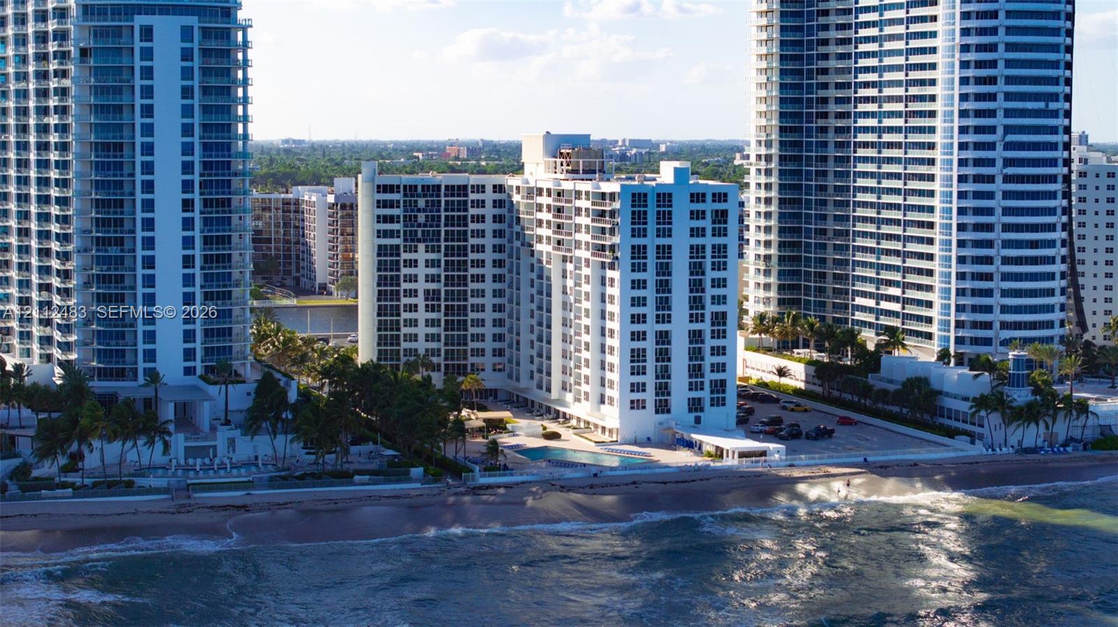 High-rise multi-story building exterior with balcony access, ground-level swimming pool, and direct coastal frontage