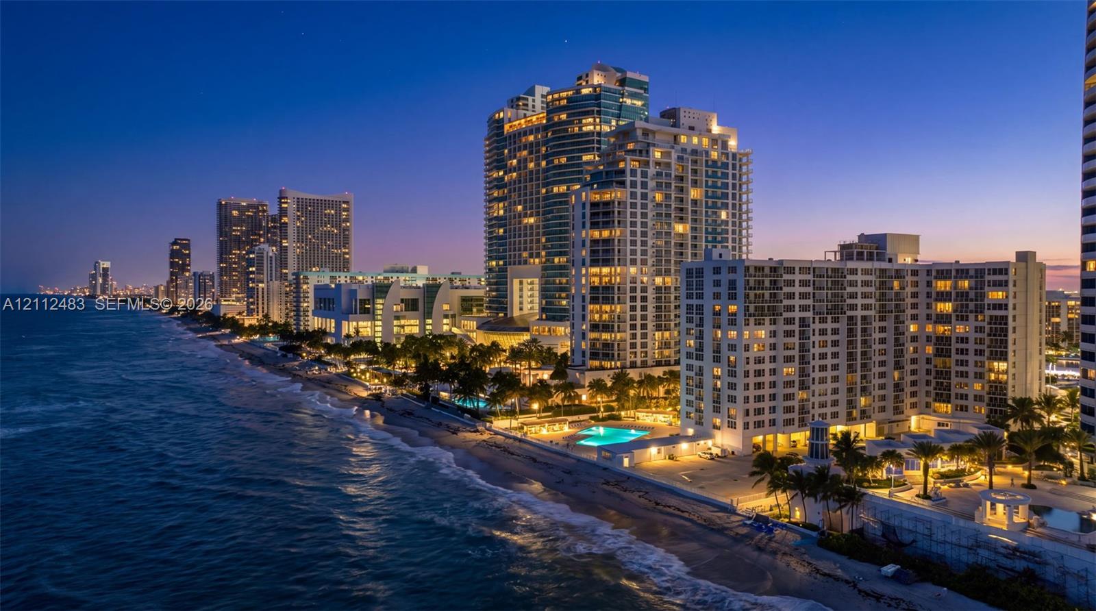 High-rise residential tower featuring direct oceanfront access, exterior balconies, landscaped grounds, and a paved pool deck with outdoor swimming pool