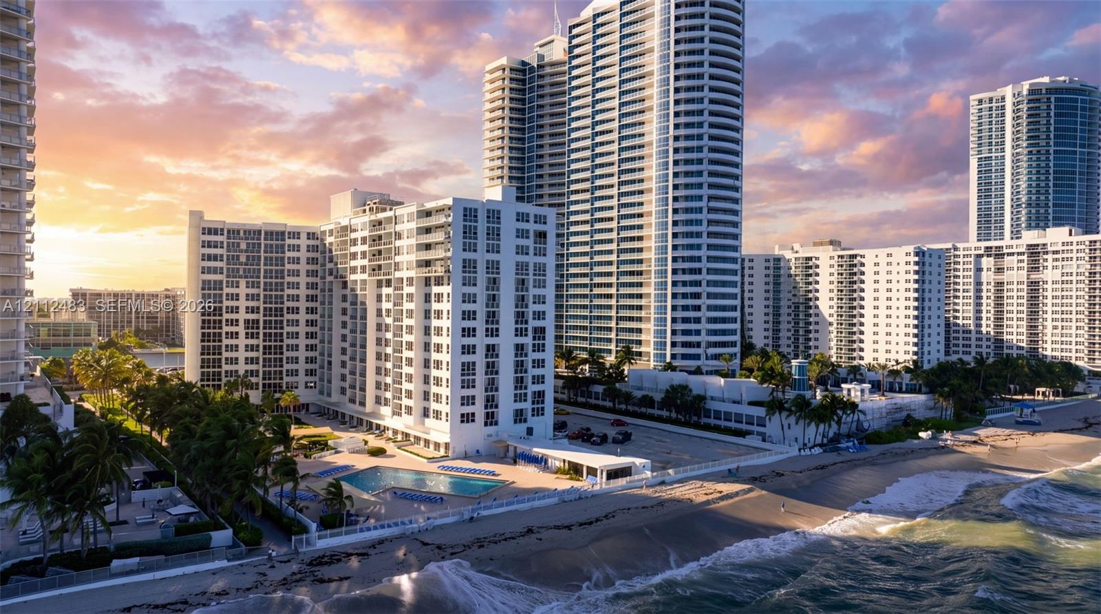 High-rise residential tower featuring a multi-story glass facade, an outdoor swimming pool, direct coastal frontage, and surface parking