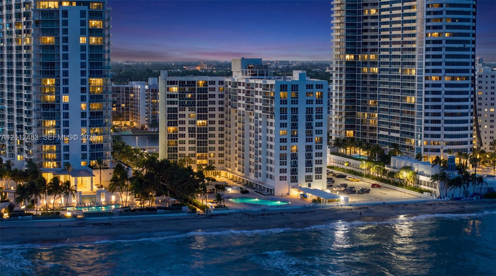 High-rise residential exterior with direct oceanfront access, exterior balconies, and a ground-level swimming pool