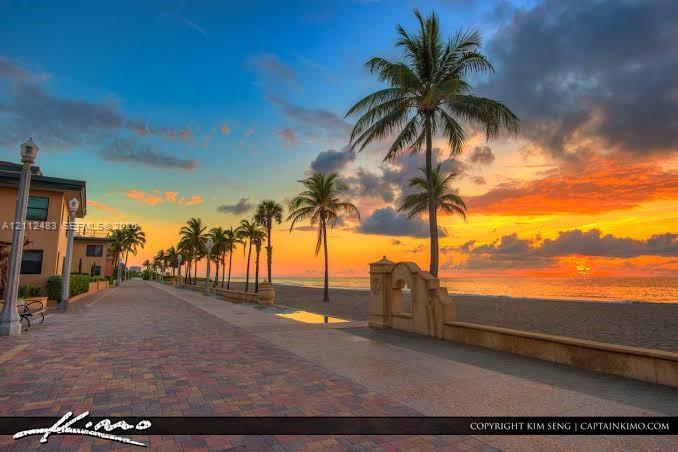 Brick-paved promenade featuring decorative lamp posts, concrete retaining walls, and mature palm trees