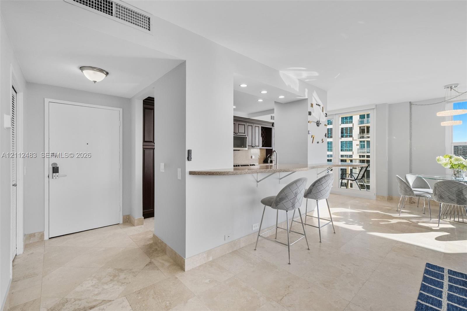 Open-concept interior featuring stone flooring, a kitchen pass-through counter, recessed lighting, and a glass-paneled door leading to an exterior balcony