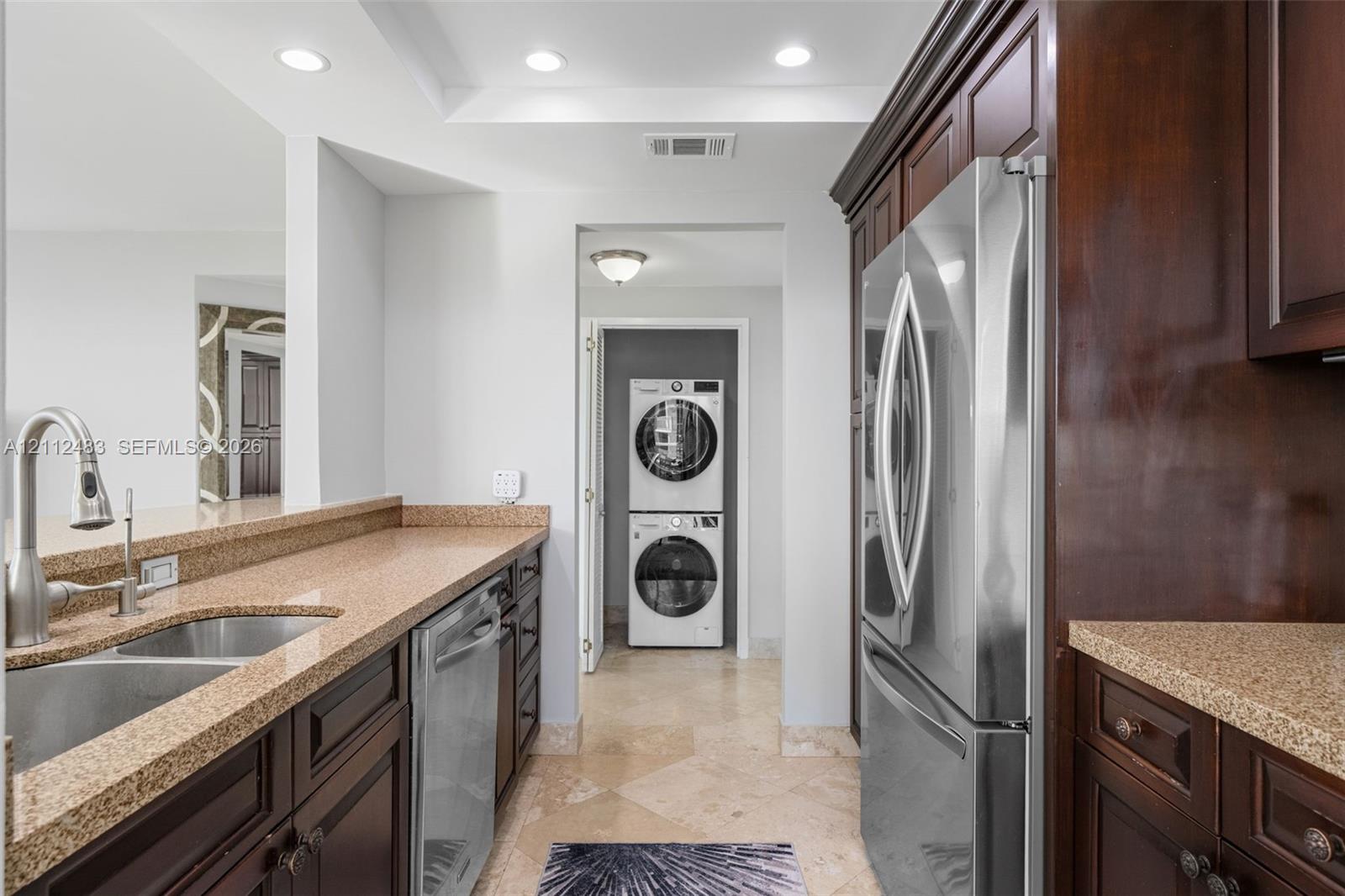 Kitchen featuring dark wood cabinetry, stone countertops, stainless steel appliances, a dual-basin undermount sink with a gooseneck faucet, and tile flooring
