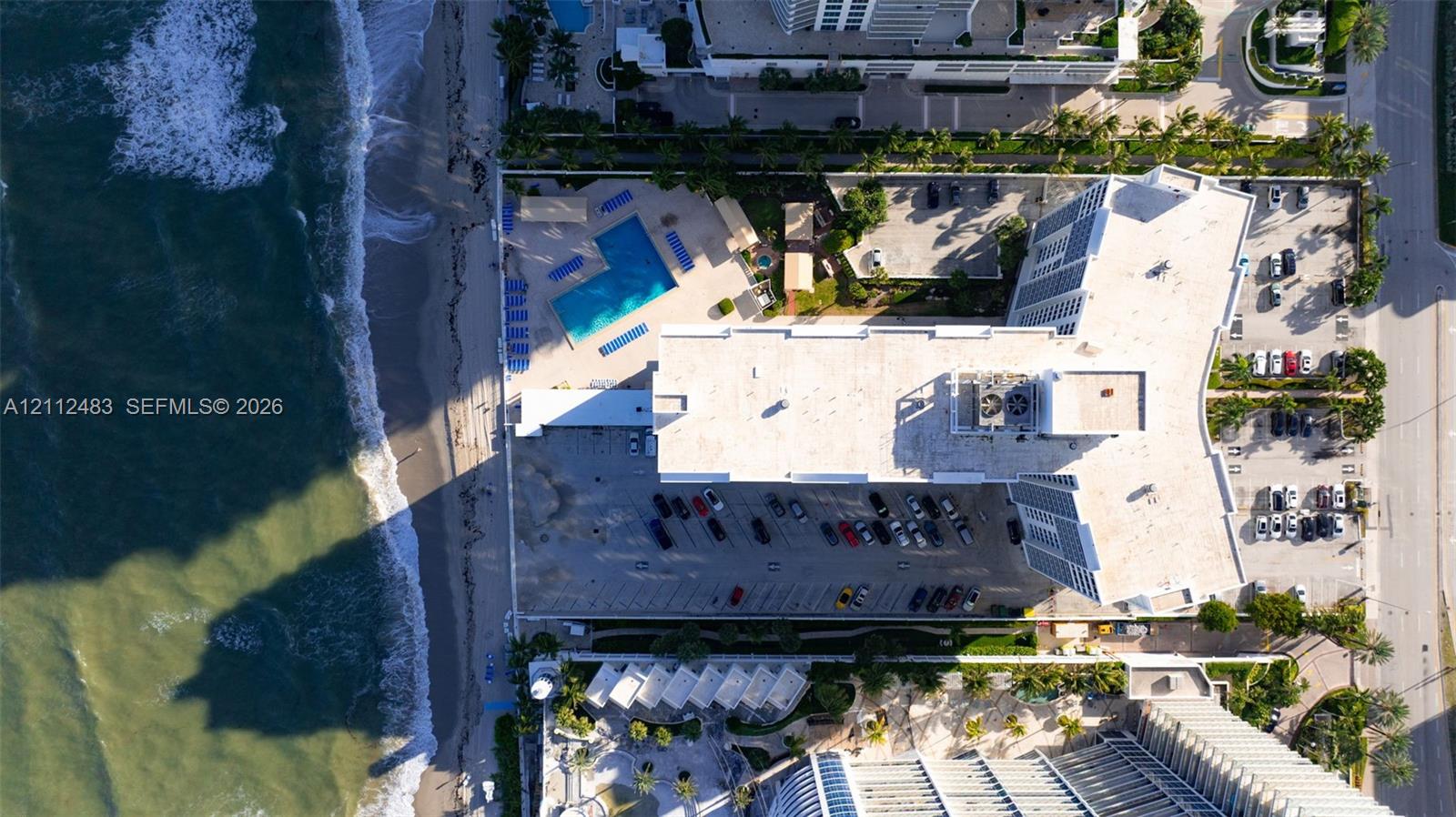 Oceanfront high-rise building featuring a swimming pool, paved surface parking, and direct beach access